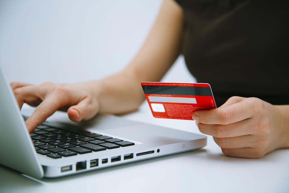 Persons hand holding a credit card and the side of their laptop as they shop online.